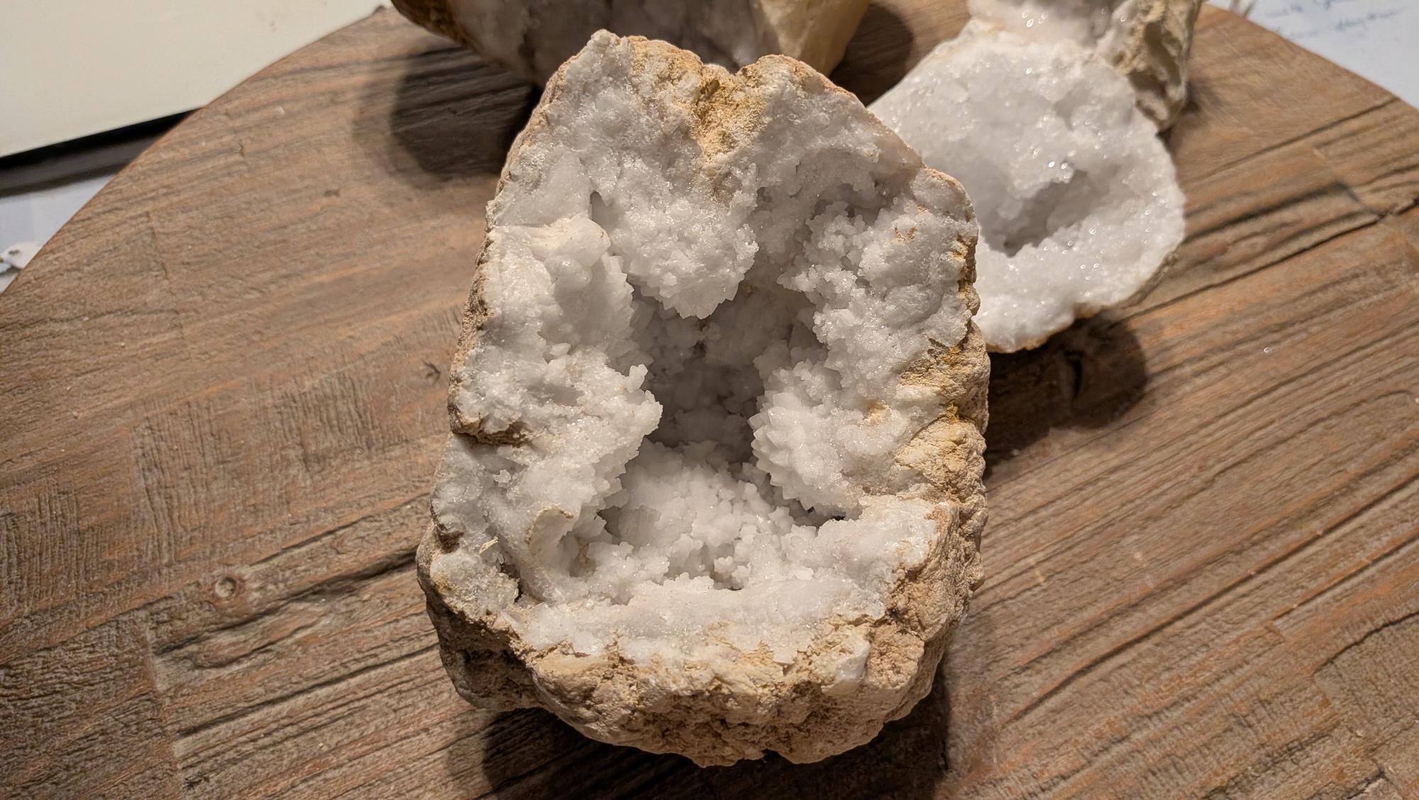Grote, zware witte kristalgeode van 1313 gram met een diepe holte vol glinsterende kristallen, gepresenteerd op een houten tafel.