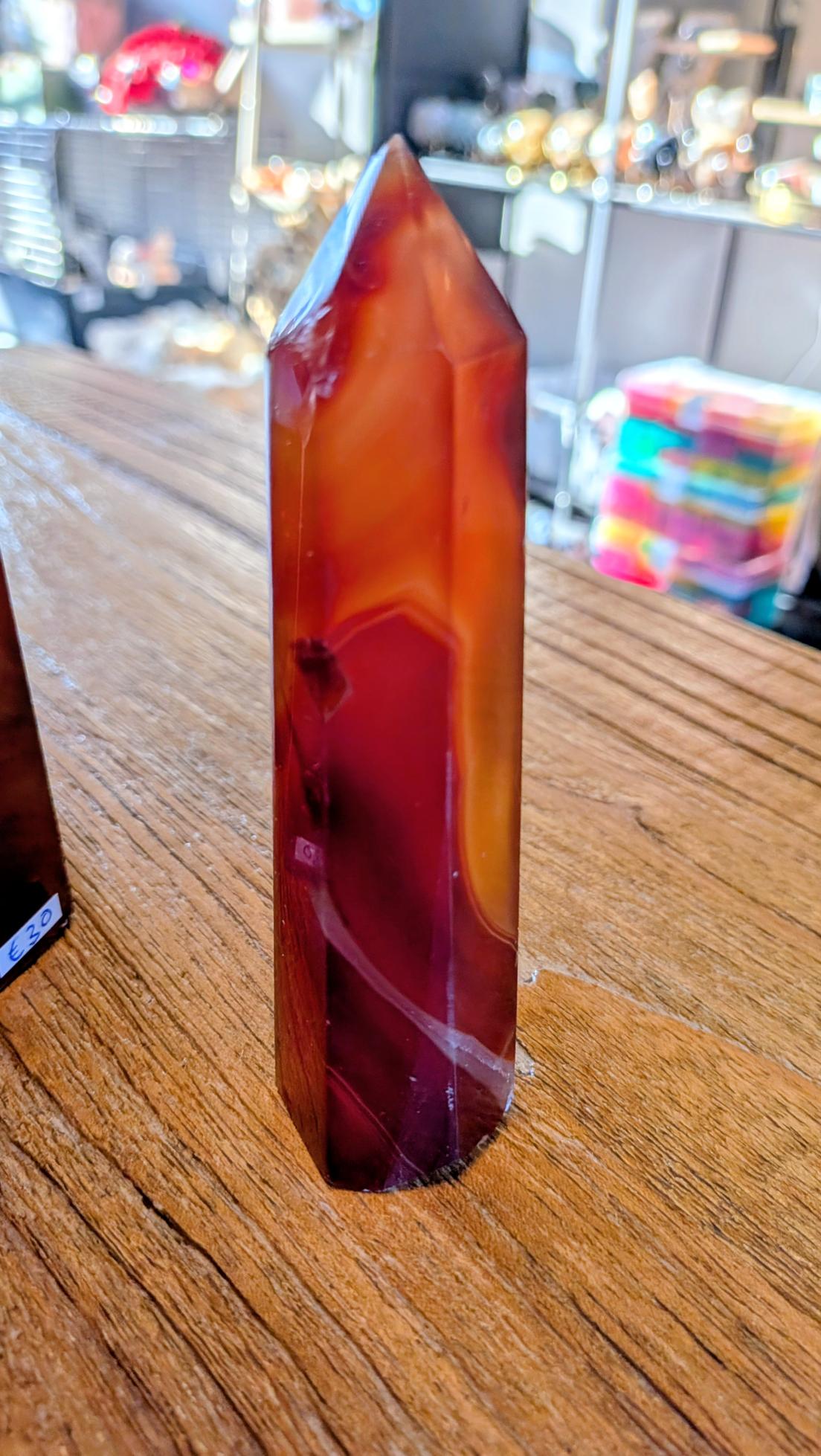 "Zijaanzicht van een gepolijste carneool punt van 157 gram op een houten ondergrond."