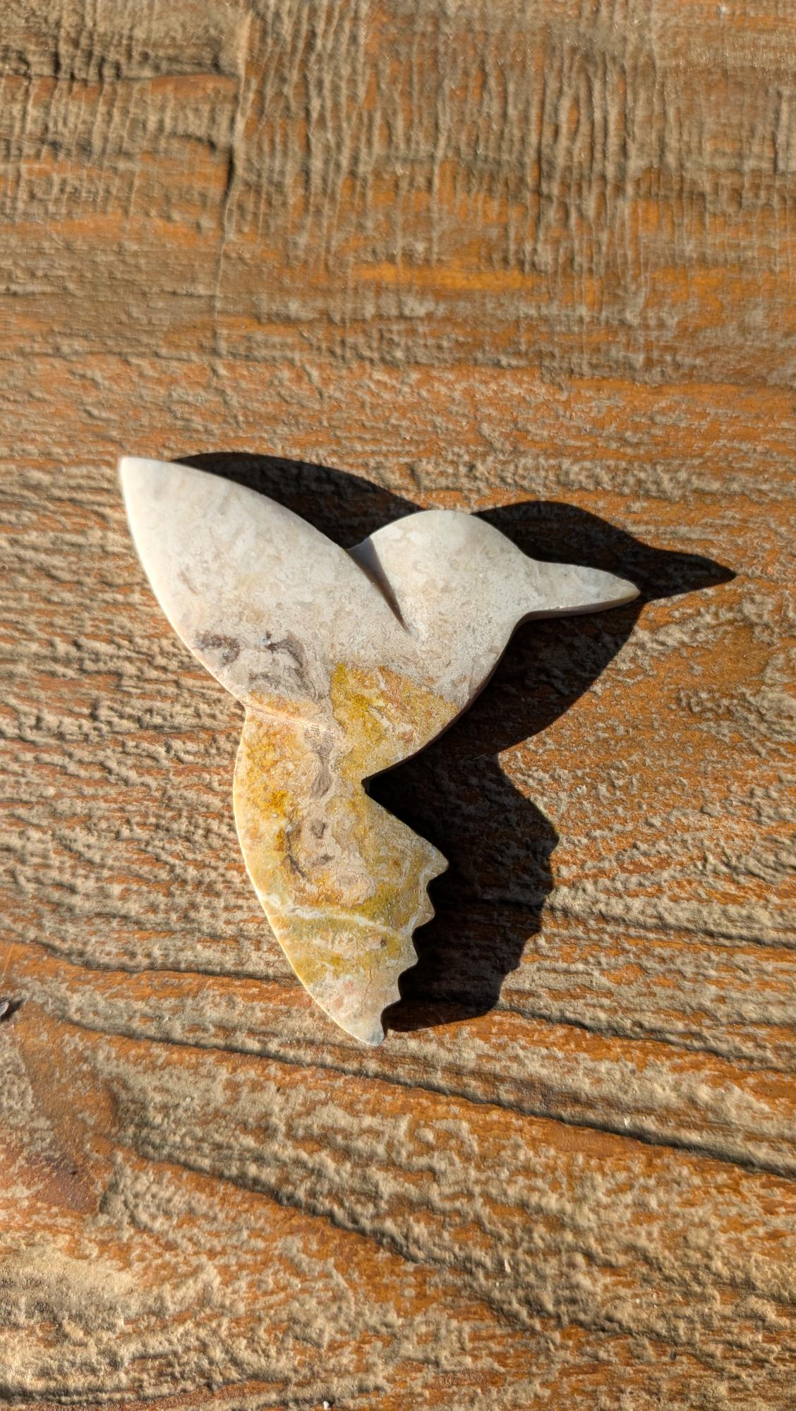 Handgesneden vogel van geel-zwarte Bumblebee Jaspis uit Java, bovenaanzicht op een houten ondergrond, formaat 5x5 cm.