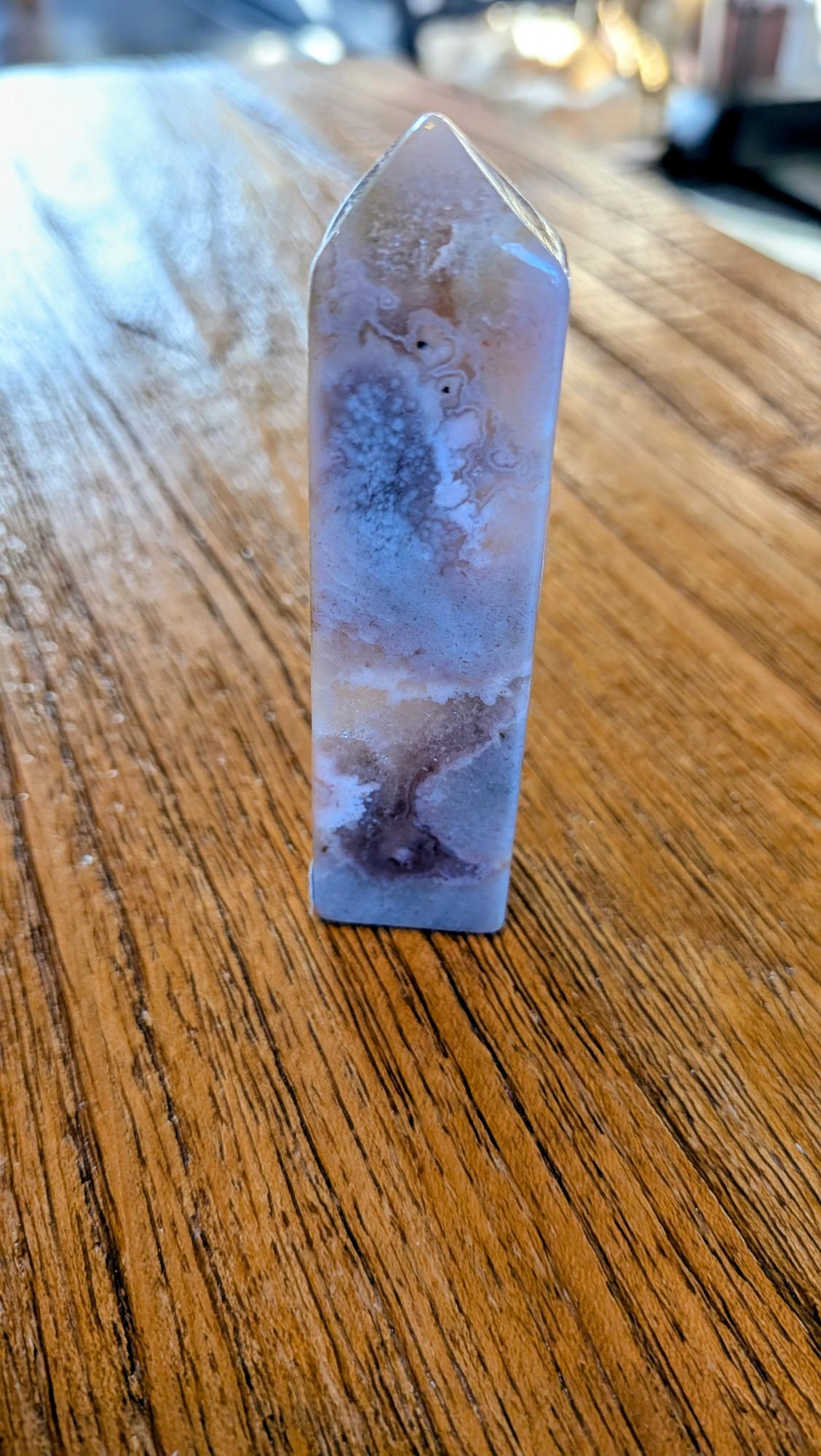 Verticale Bloem Agaat kristal toren van 8 cm hoog met witte bloesemachtige patronen op een houten ondergrond.