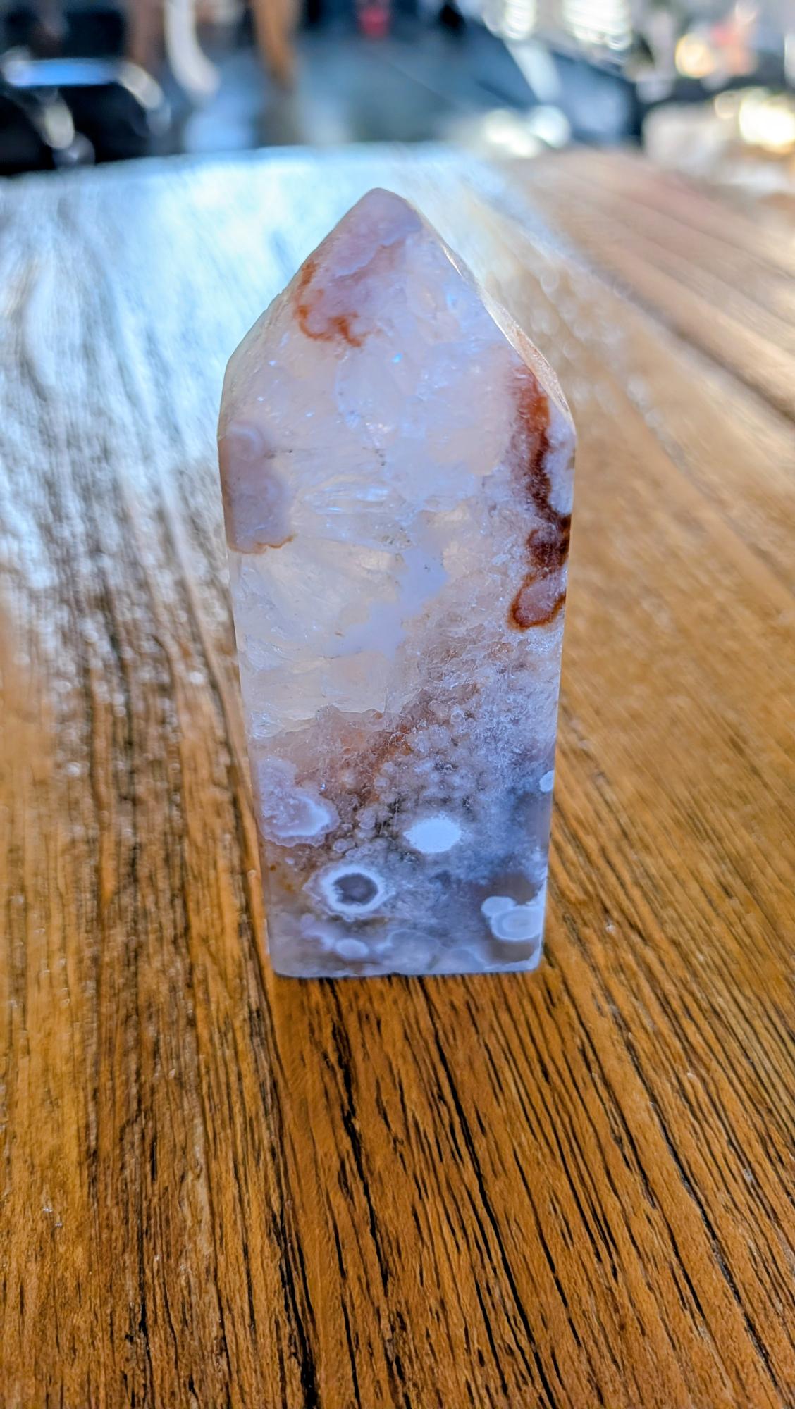 Verticale Bloem Agaat kristal toren van 8,5 cm met witte chalcedoon bloemen en rode kleuraccenten op een houten achtergrond.