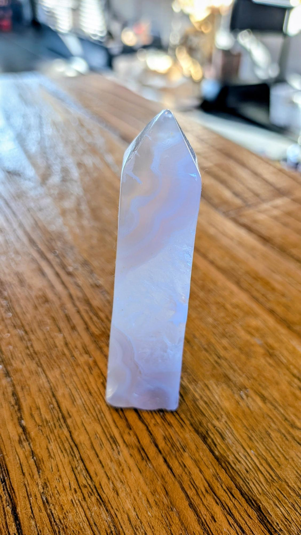 Verticale Bloem Agaat kristal toren van 8 cm met zachte roze-grijze kleuren en witte bloemvormige insluitingen op een houten ondergrond.