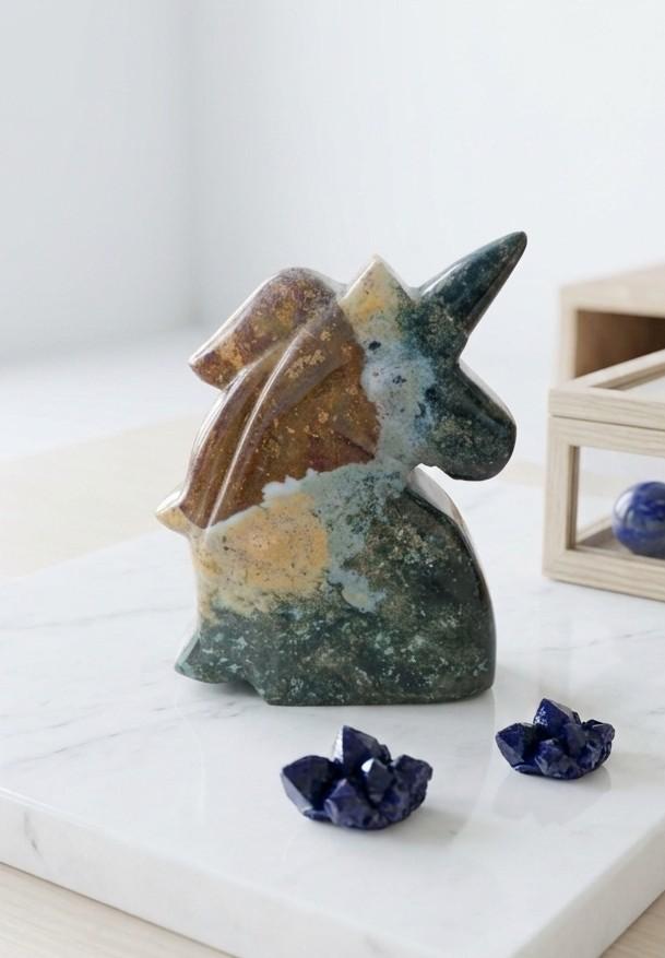 Handgesneden eenhoorn van groen-bruine Jaspis, ambachtelijk gemaakt op Java, op een marmeren plateau.