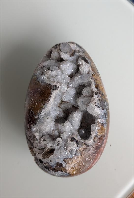 Een gepolijst rood jaspis ei met een grote open holte vol sprankelende witte druzy kristallen.