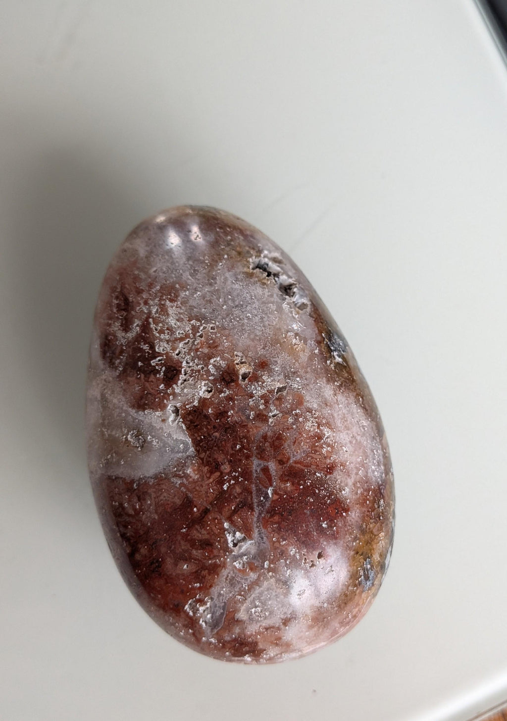 Een gepolijst rood jaspis ei met een grote open holte vol sprankelende witte druzy kristallen.