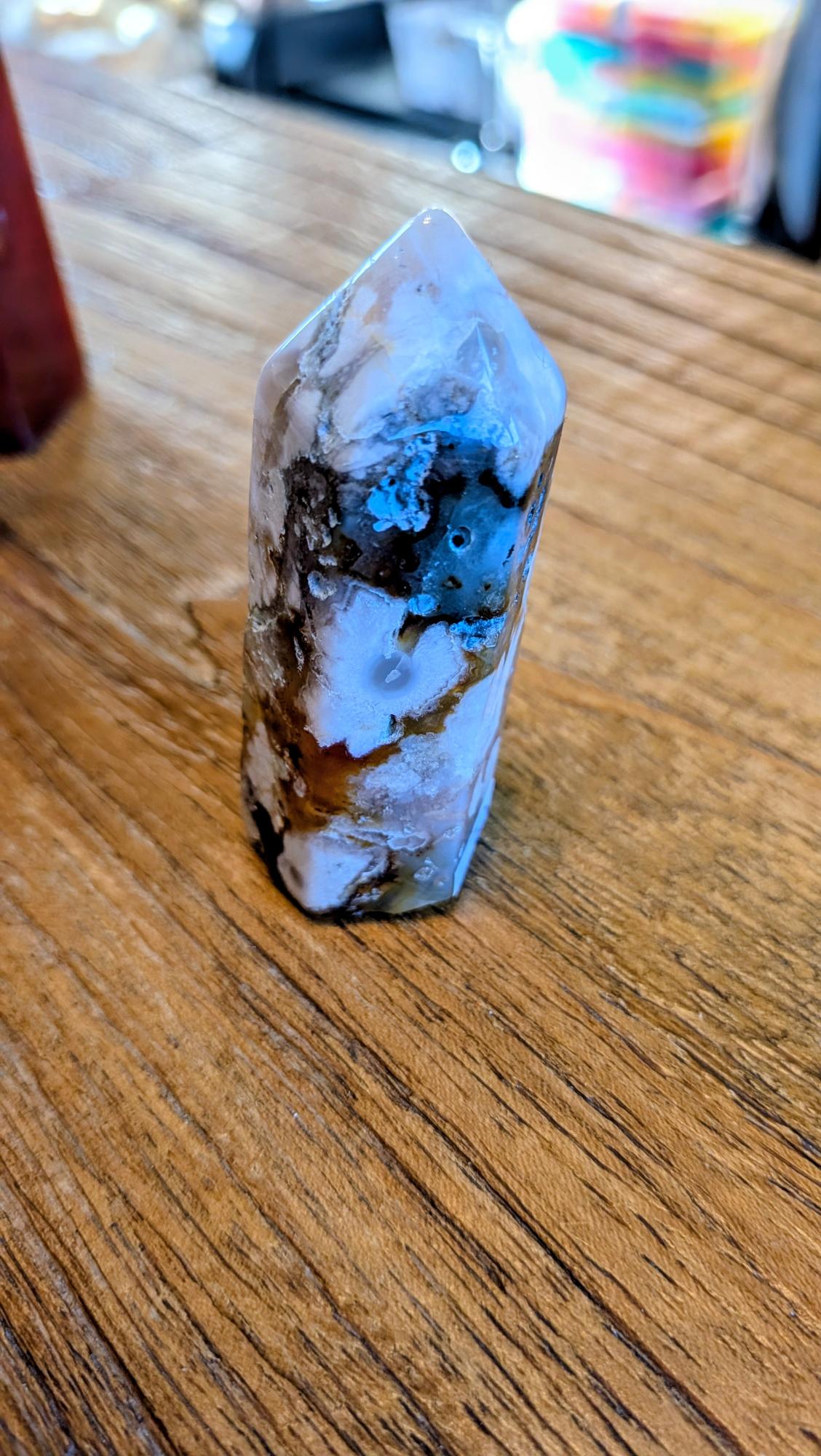 Stevige Bloem Agaat kristal toren van 7 cm hoog met witte bloemtekeningen en 70 gram gewicht op een houten achtergrond.