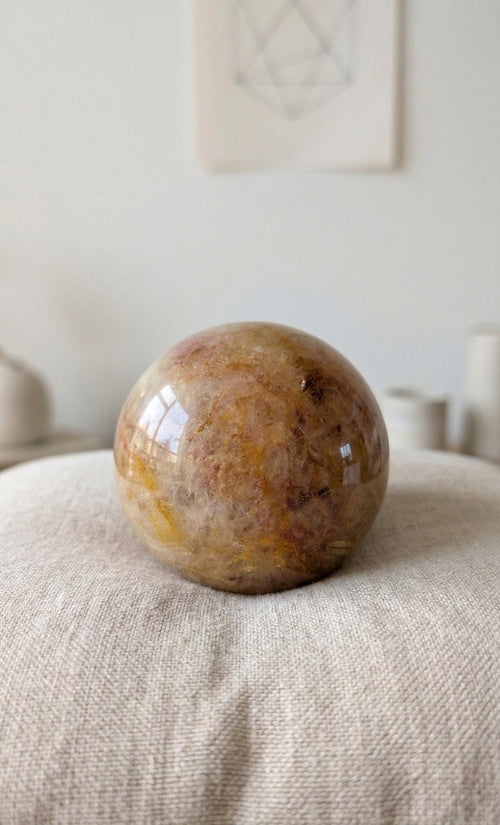 Gepolijste Golden Healer Kwarts bol van 5 cm met goudgele insluitingen op een wit linnen kussentje. Kristal voor genezing en positiviteit.