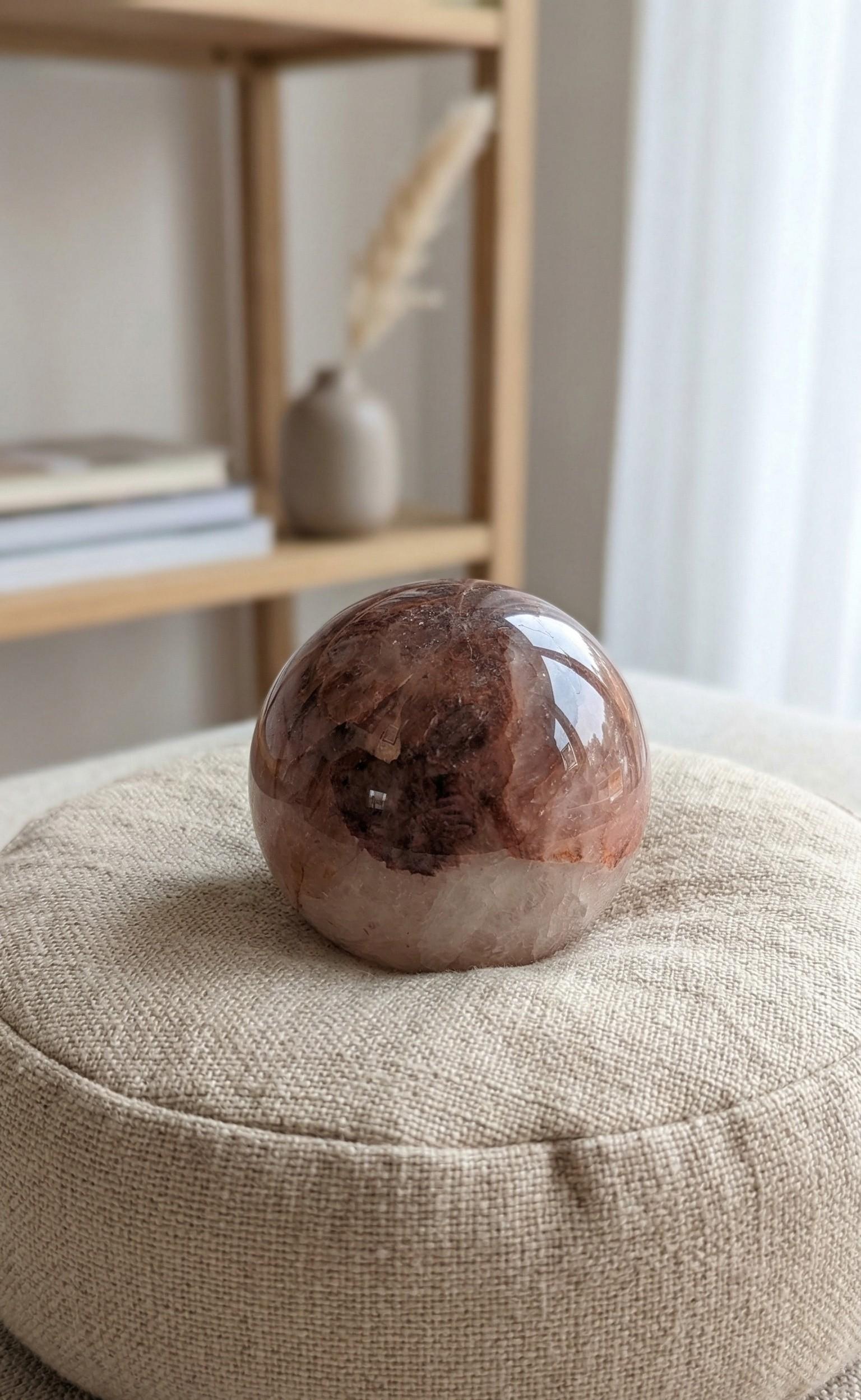 Gepolijste Fire Quartz bol van 7 cm met dieprode hematiet insluitingen op een linnen kussentje. Kristal voor focus en vitaliteit.