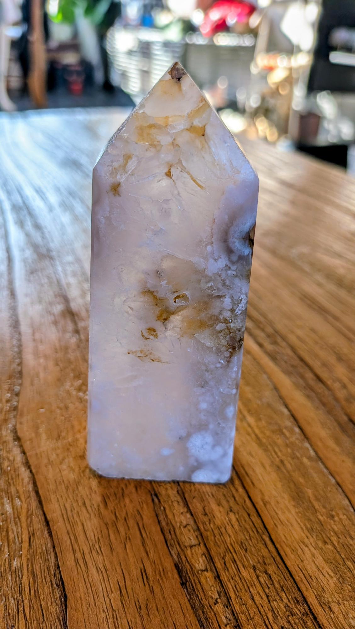 "Gepolijste Bloemagaat toren met witte bloemachtige patronen in een lichtroze en witte kristalstructuur, staand op een houten ondergrond."