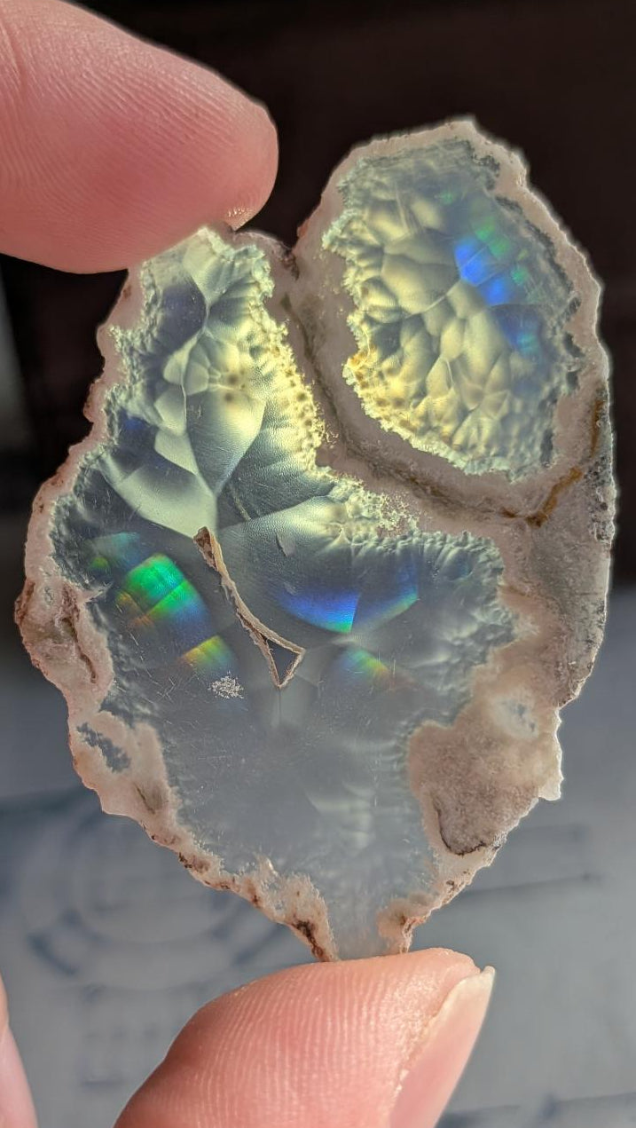 Iris Agaat uit Java (5,5 cm) met een organische vorm en felle blauw-groene regenboogkleuren die oplichten tegen een sterke lichtbron.