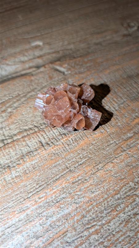 Klein roodbruin Aragoniet Sputnik kristal van 21 gram met duidelijke zeshoekige kristalpunten op een houten ondergrond.
