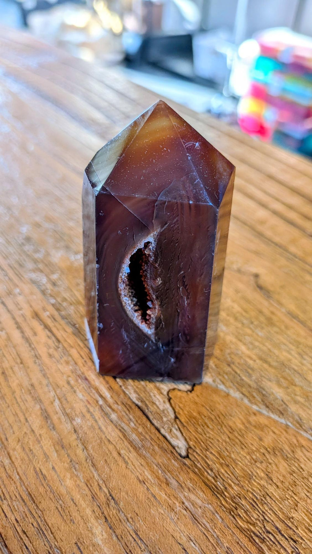 "Donkeroranje Carneool kristal tower met een opvallende inkeping/beschadiging staand op een houten tafel."