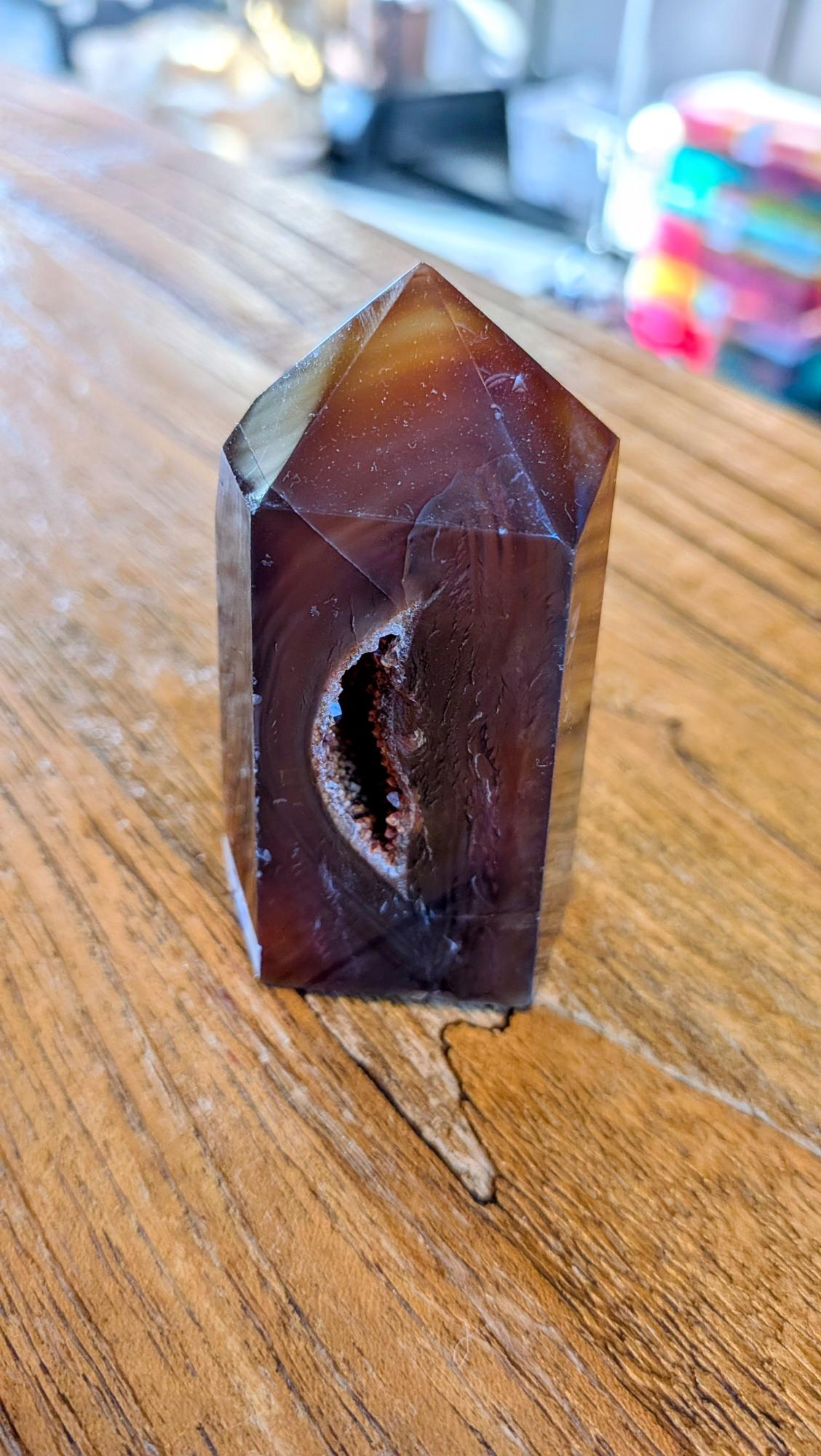 "Donkeroranje Carneool kristal tower met een opvallende inkeping/beschadiging staand op een houten tafel."