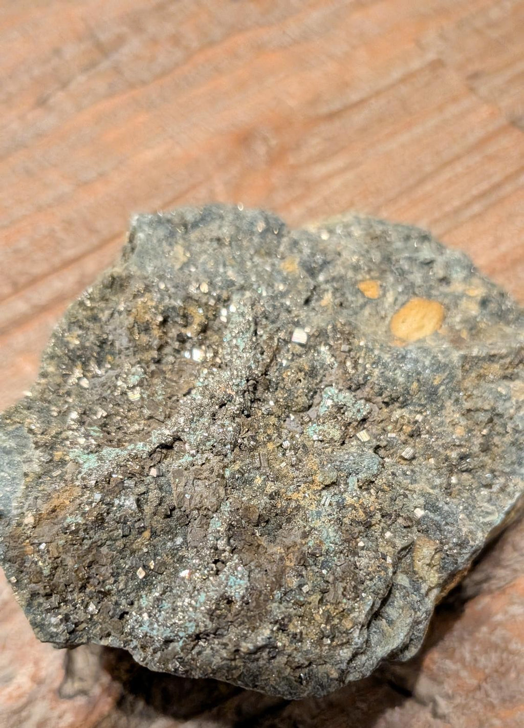 Goudkleurige Pyriet kristallen op een donkergrijze matrix steen van 264 gram op een houten ondergrond.