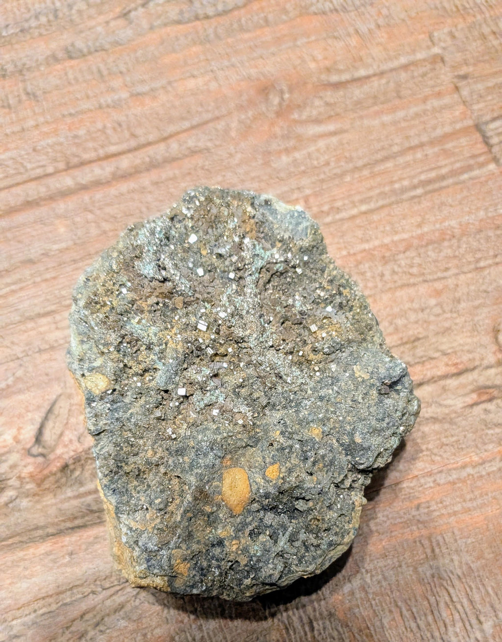 Goudkleurige Pyriet kristallen op een donkergrijze matrix steen van 264 gram op een houten ondergrond.