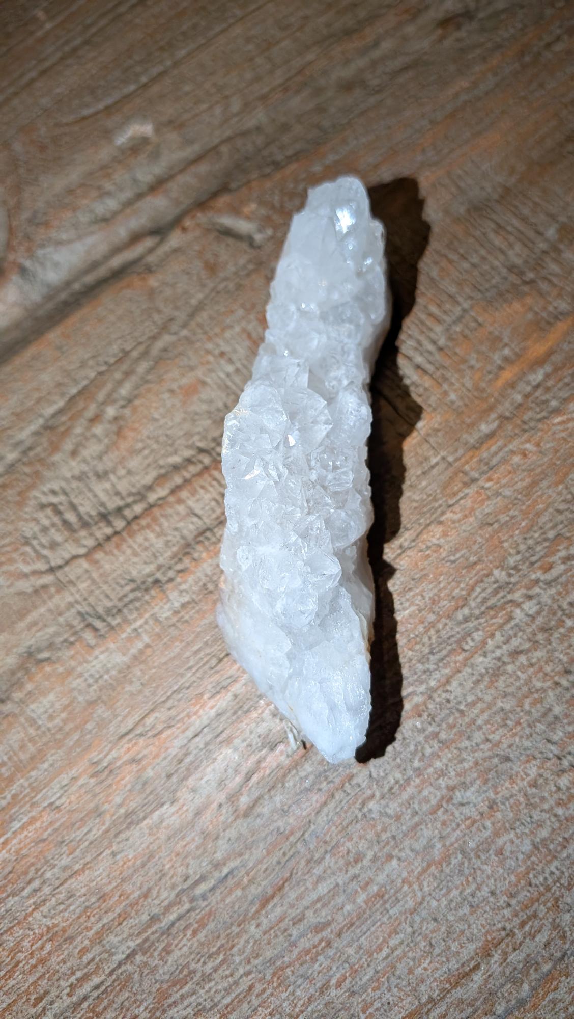 Helder wit Bergkristal cluster van 74 gram met diverse kleine kristalpunten op een houten achtergrond.