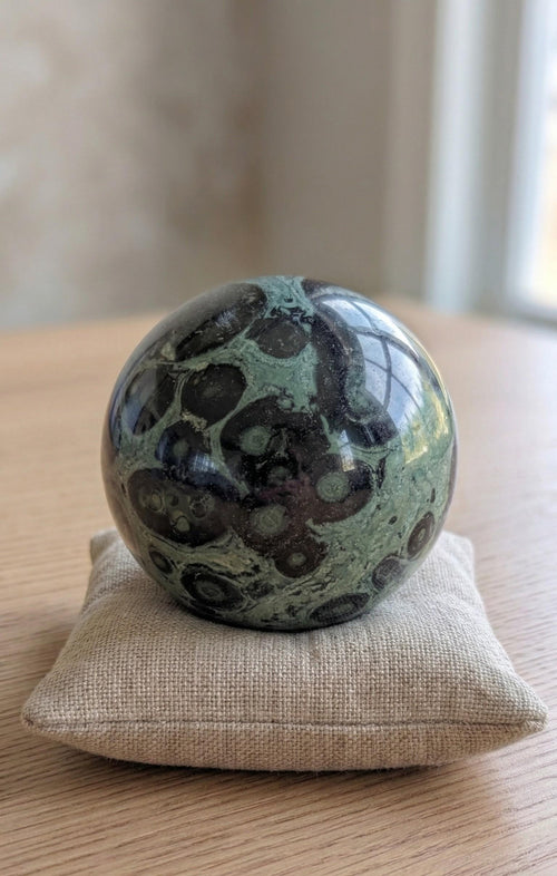 Grote gepolijste groene Kambaba Jaspis bol van 7 cm met zwarte cirkelpatronen op een kussentje, prijs 42,50 euro. Houders apart verkrijgbaar.