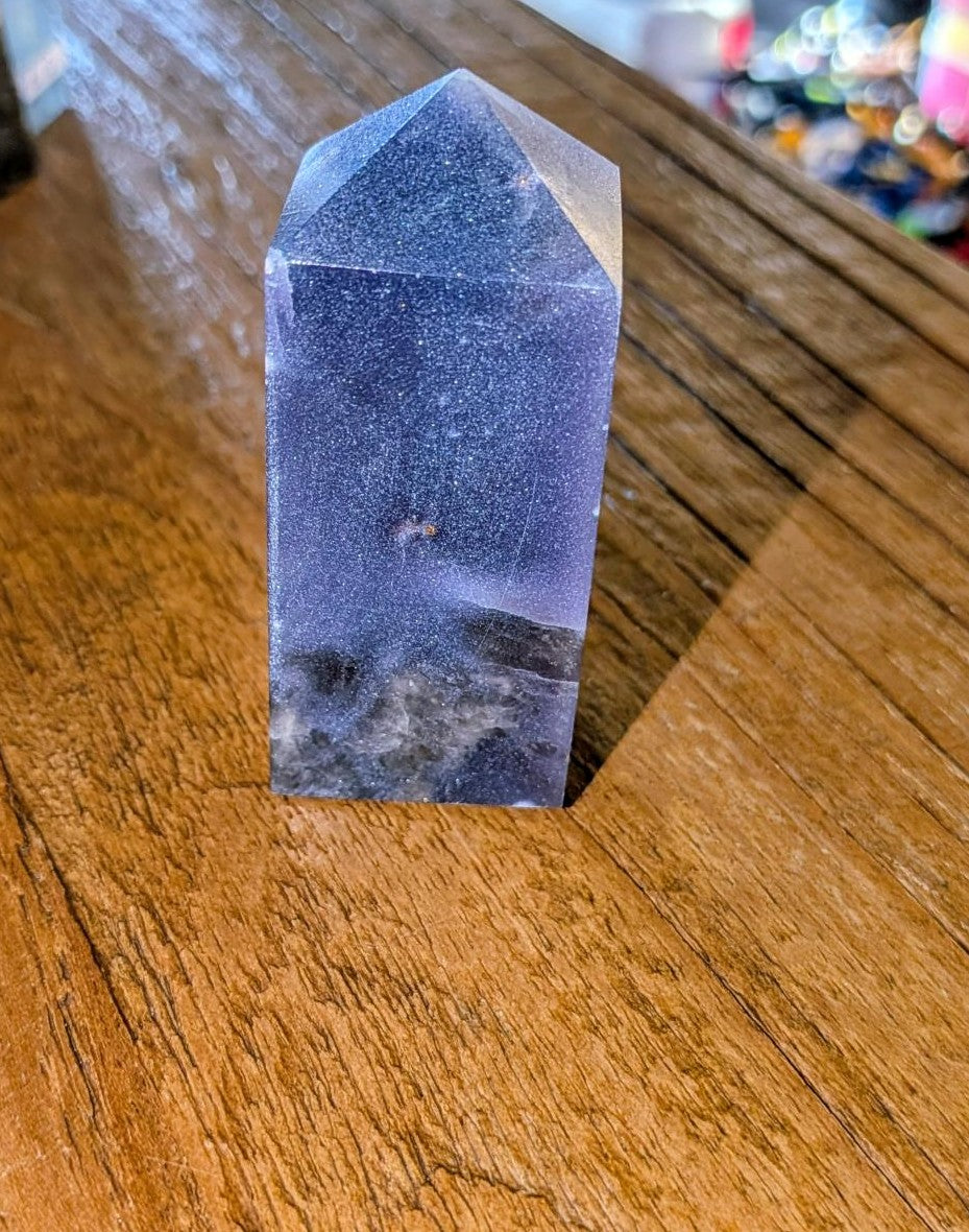 "Gepolijste paarse Lepidoliet kristal toren met natuurlijke zilveren glinsteringen, staand op een houten ondergrond."