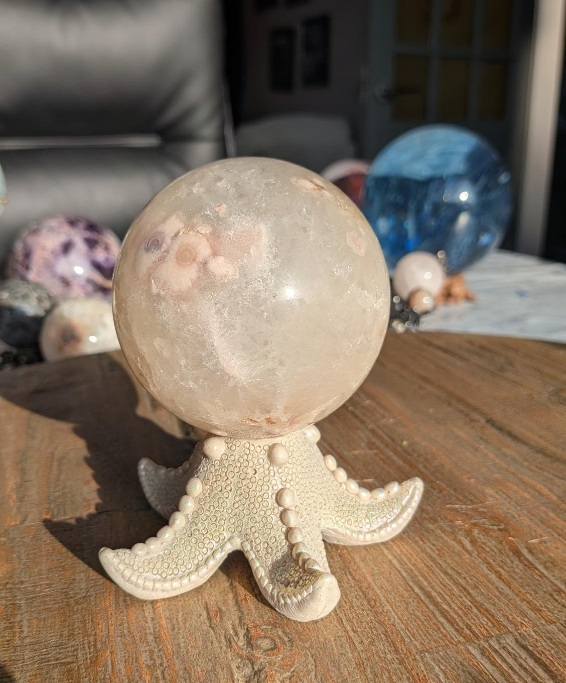 Een grote Kersenbloesem agaat bol met duidelijke bloempatronen op een witte zeester houder met parelmoerglans, geplaatst op een houten ondergrond.