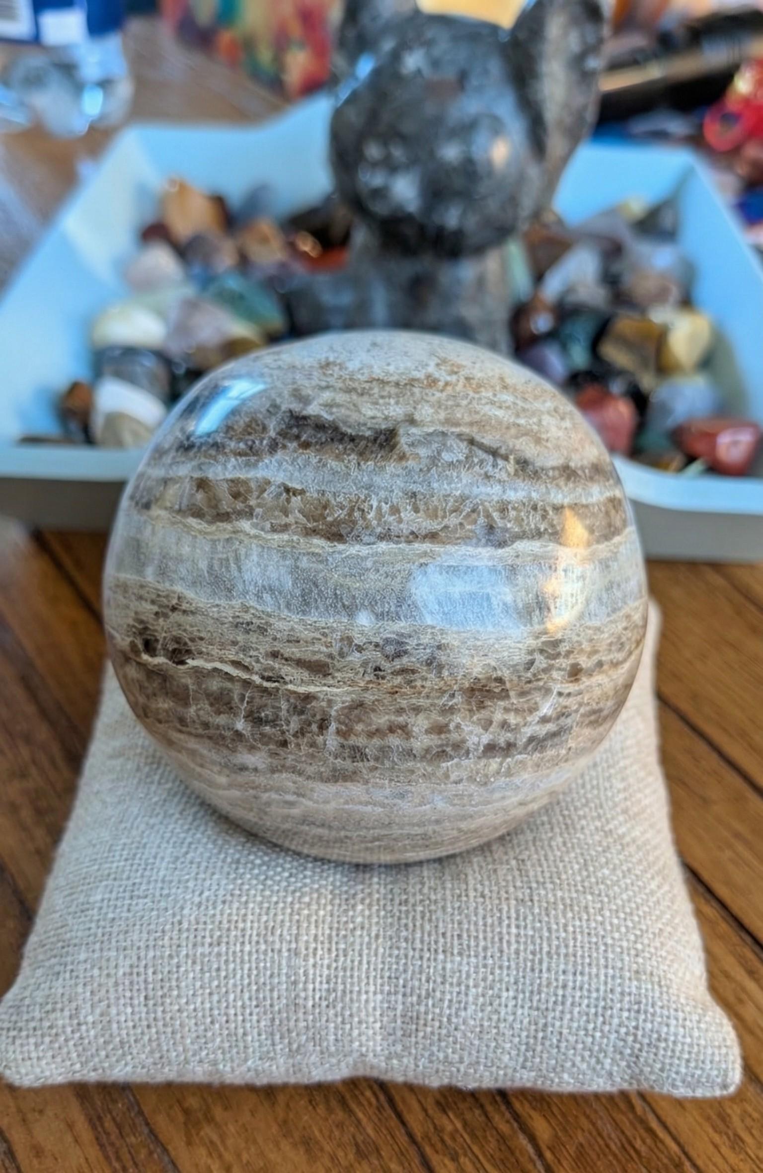 Grote gepolijste Mica Calciet bol van 8 cm met bruine banden en glinsteringen op een burlap kussentje, prijs 54,95 euro. Houders apart verkrijgbaar.