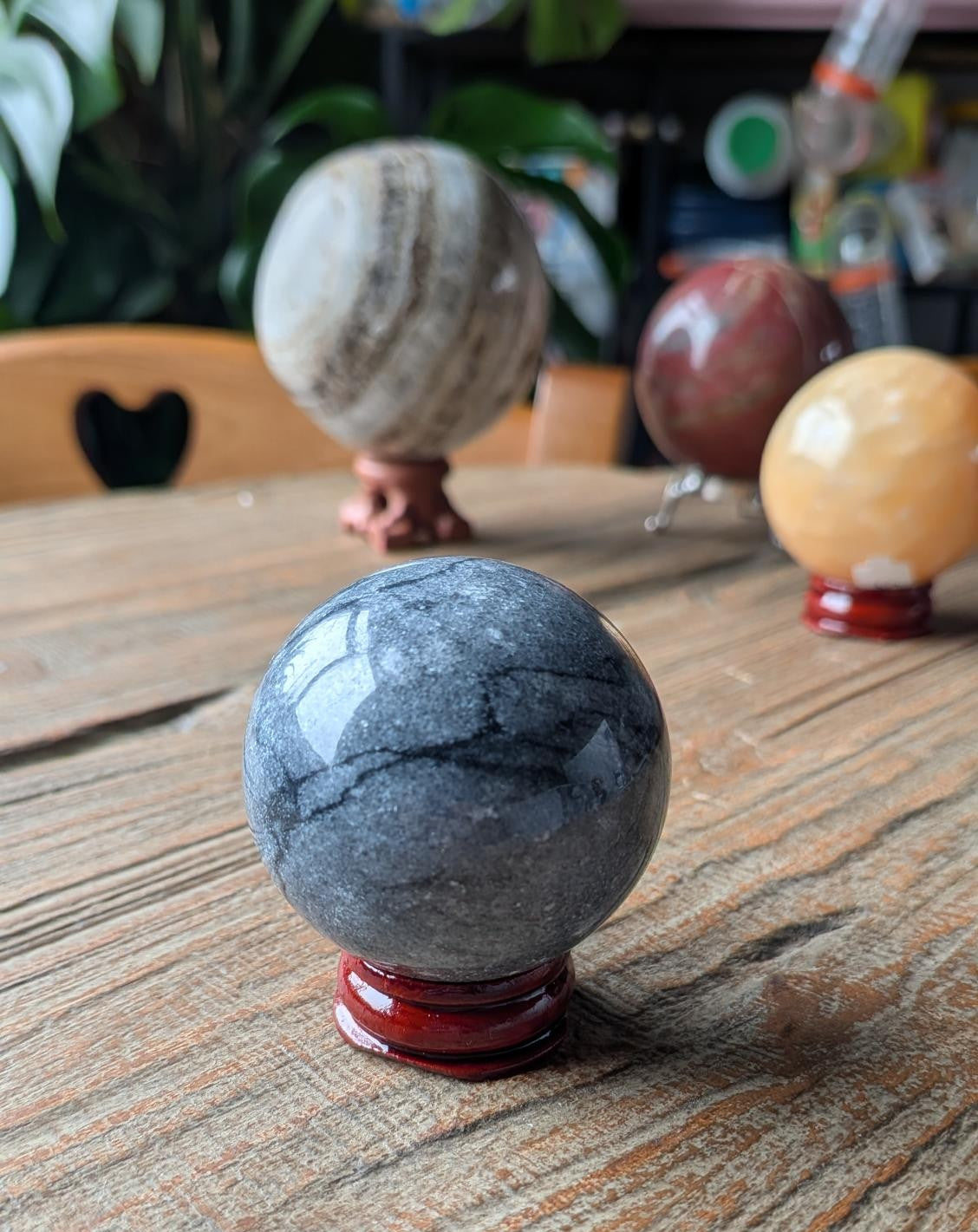 Een massieve, diepdonkere jade bol van 4.5 cm, glad gepolijst en rustend op een eenvoudige houder tegen een neutrale achtergrond.