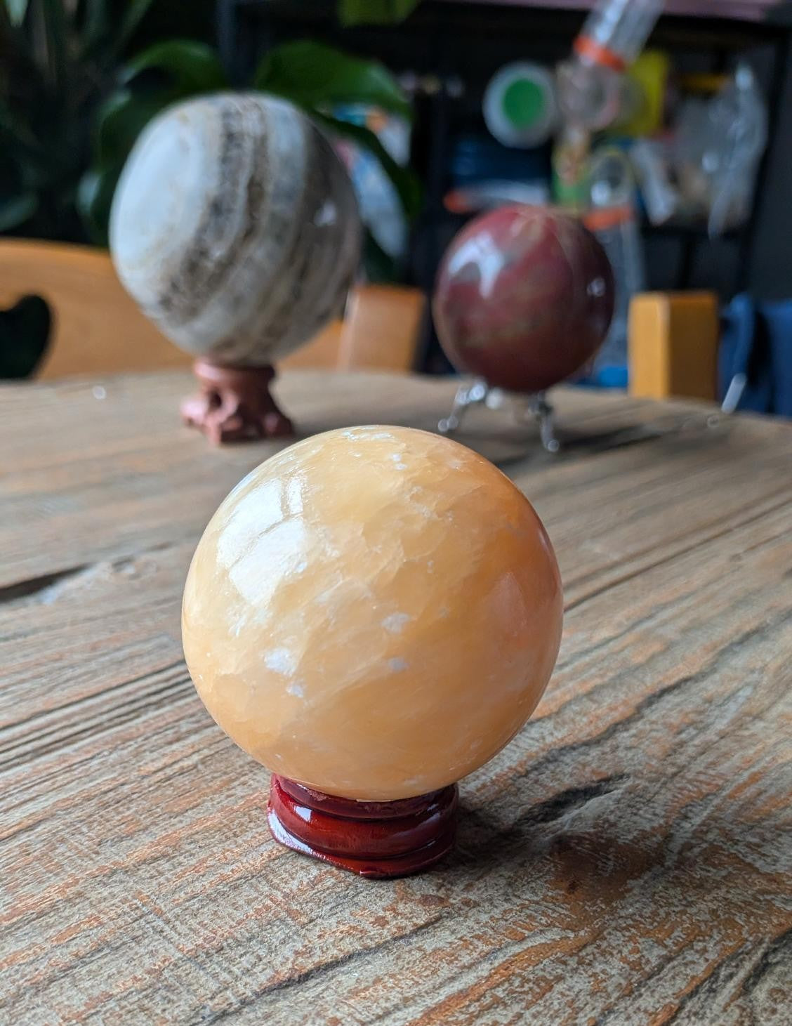 Een glanzende, feloranje calciet bol van 5 cm diameter, rustend op een eenvoudige houder op een houten ondergrond in natuurlijk daglicht.