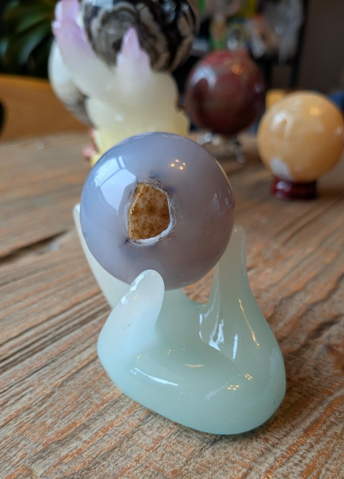 Gepolijste Agaat bol van 4 cm met een glinsterende druzy holte, gepresenteerd op de meegeleverde houder op een houten tafel.