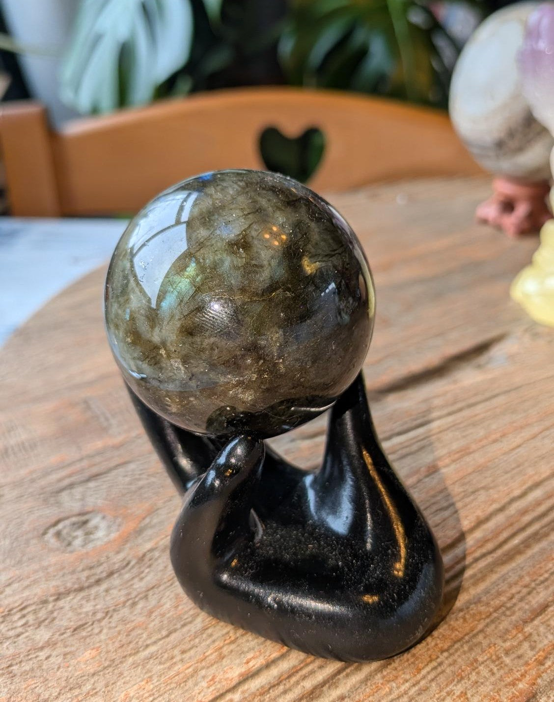 Gepolijste Labradoriet bol van 5 cm met blauwe glans, rustend in een zwarte decoratieve hand-houder.