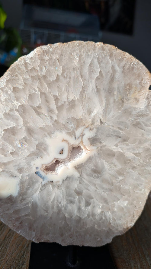 Een grote, ronde witte kristalschijf van agaat met een centrale holte, gemonteerd op een modern zwart metalen statief.