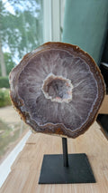 Een hand houdt een grote Agaat-geode van 1237 gram op een zwarte standaard vast, met zicht op het kristalhart