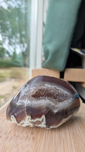 Een hand houdt een elegante Agaat-geode van 333 gram vast, met een diepe kleur en een schitterend kristalhart in het midden