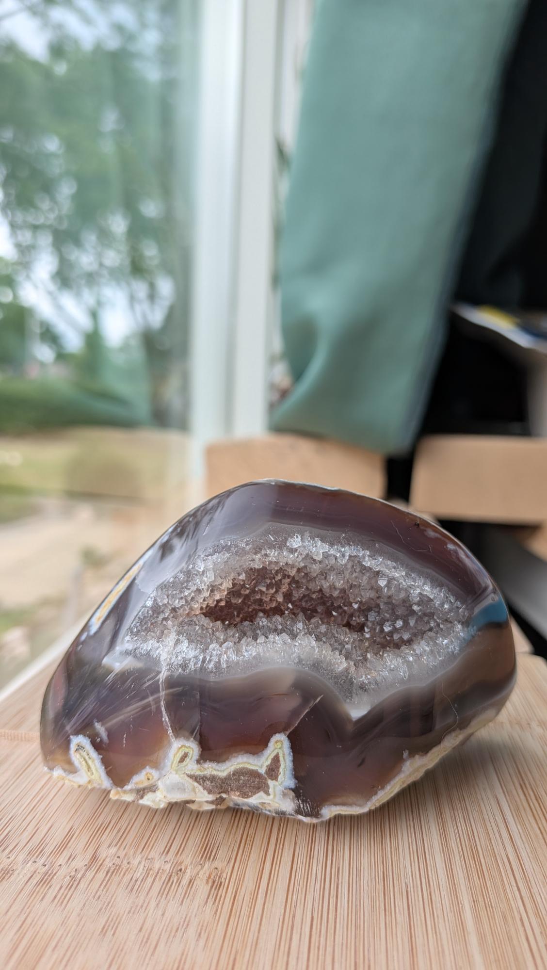 Een hand houdt een elegante Agaat-geode van 333 gram vast, met een diepe kleur en een schitterend kristalhart in het midden