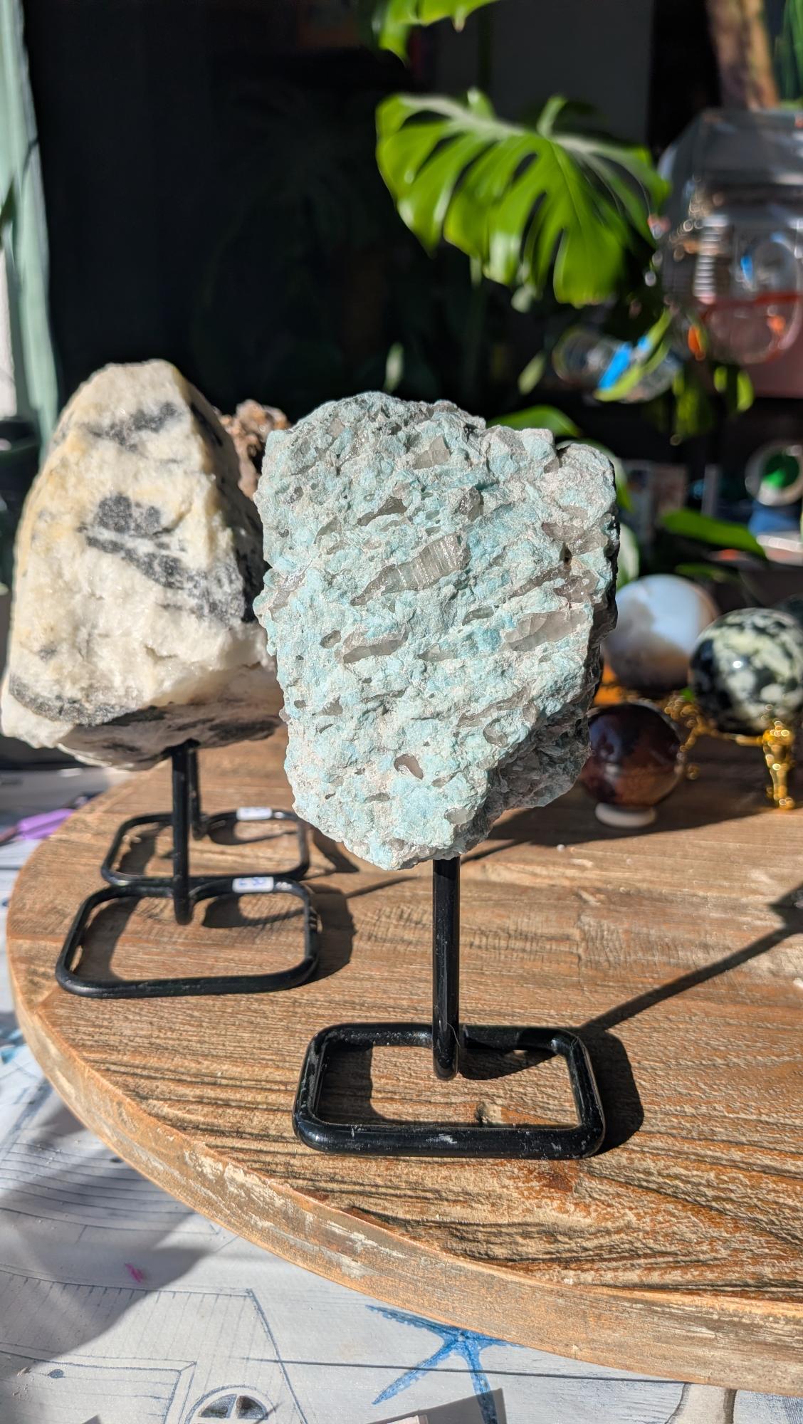 Ruwe turquoise Amazoniet met ingesloten grijze Rookkwarts kristallen op een zwarte metalen standaard.