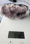 Een groot en zwaar Amethist cluster van 948 gram met dieppaarse, kristalachtige punten, gefotografeerd op een digitale weegschaal.