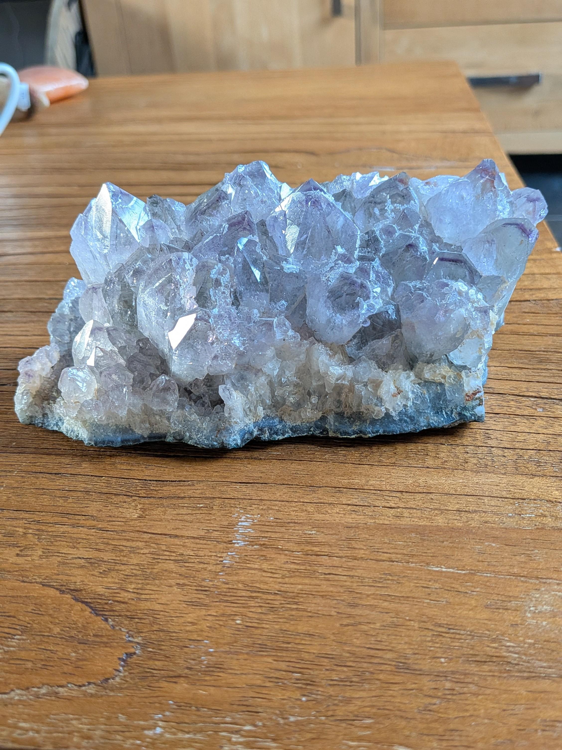 "Groot natuurlijk Amethist cluster met talloze paarse kristalpunten, 16 cm breed en 1200 gram, liggend op een houten tafel."