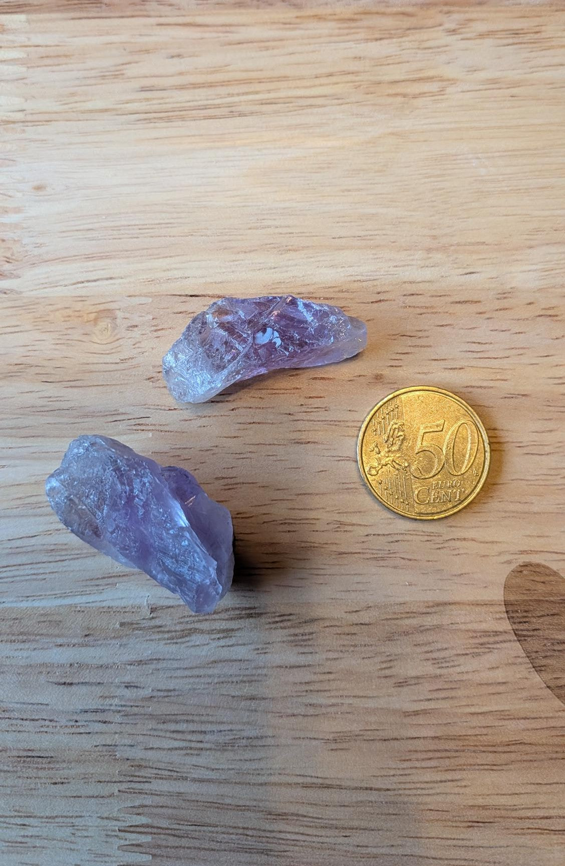 Twee ruwe paarse amethist kristallen naast een 50 eurocent munt op een houten achtergrond, klaar voor verwerking tot een custom wire wrapped hanger.