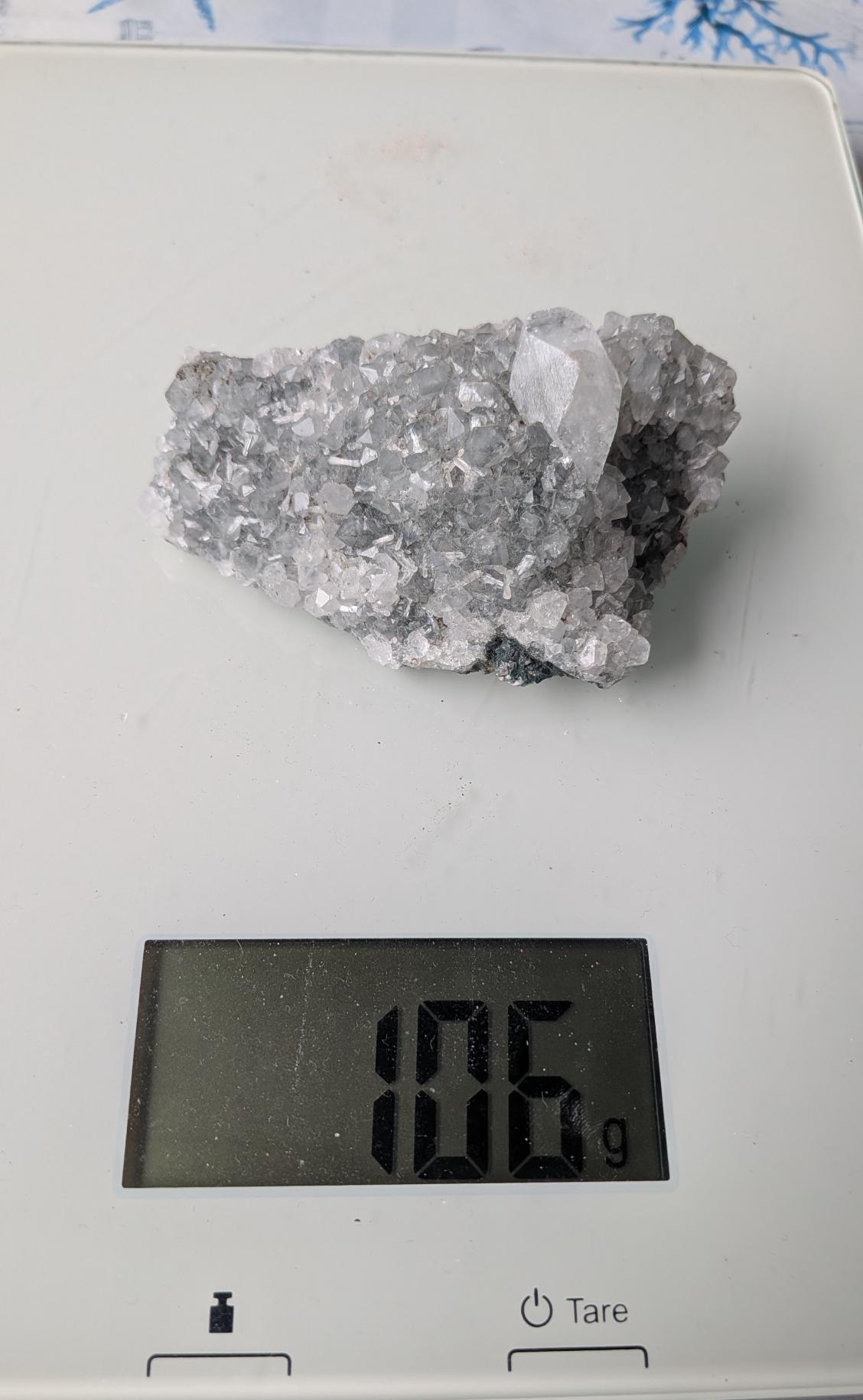 Een helder Apofylliet cluster van 106 gram met geometrische, glasachtige kristallen, gefotografeerd op een digitale weegschaal.