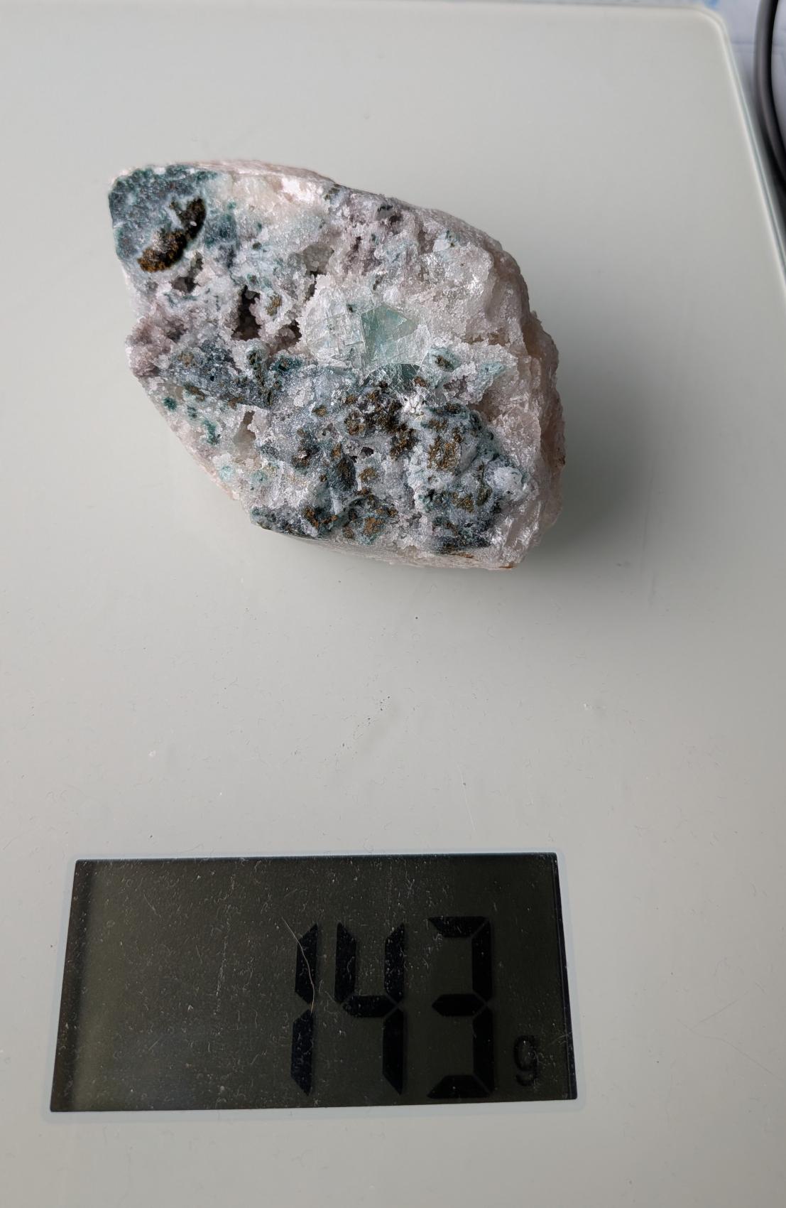Een exclusief, ruw Apofylliet cluster uit Nasik, India, met glasachtige heldere kristallen op een zachtroze Stilbiet-matrix, gewogen op een digitale weegschaal die 143 gram aangeeft.