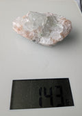 Een exclusief, ruw Apofylliet cluster uit Nasik, India, met glasachtige heldere kristallen op een zachtroze Stilbiet-matrix, gewogen op een digitale weegschaal die 143 gram aangeeft.