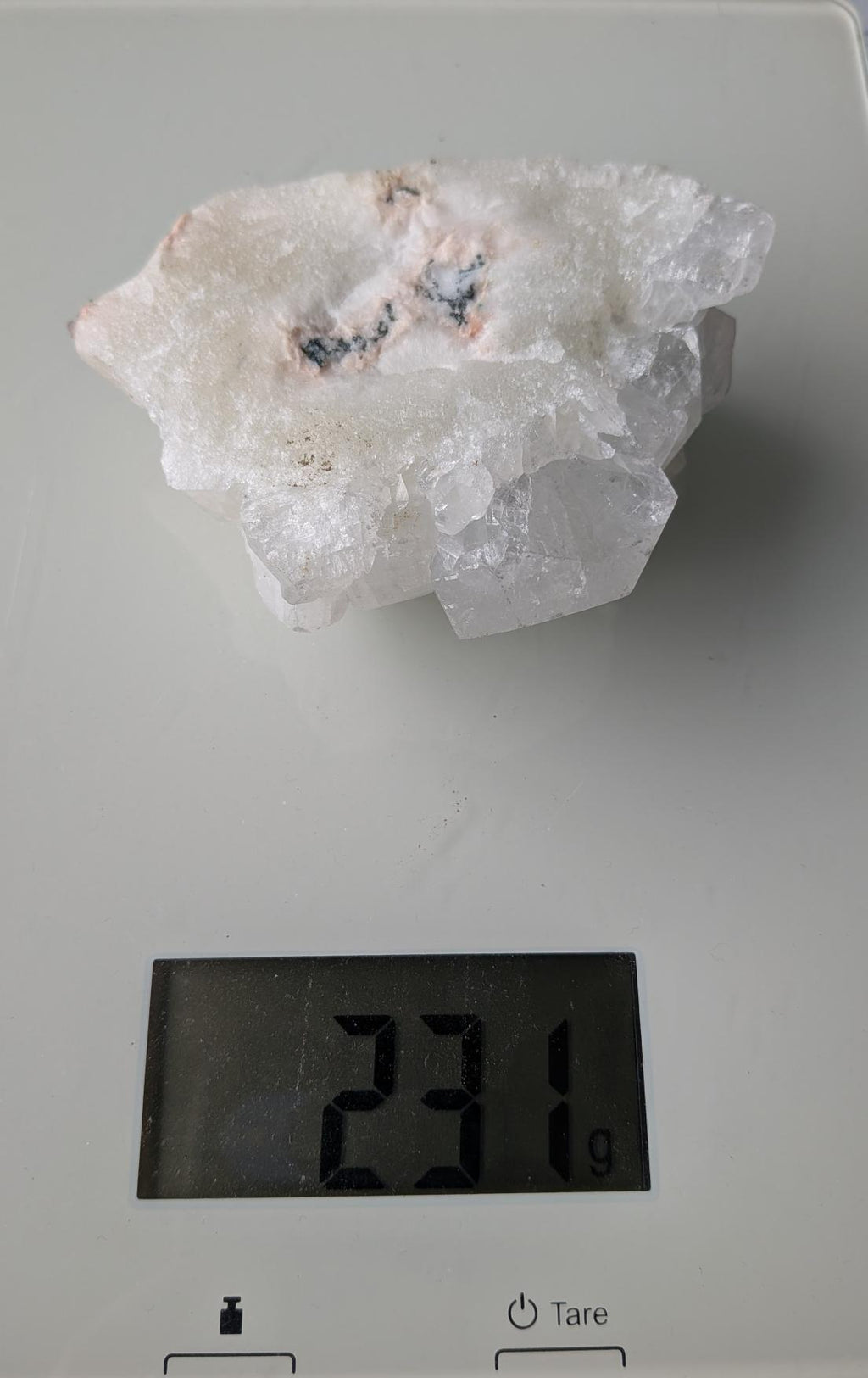 Een substantieel Apofylliet cluster van 231 gram uit Nasik, India, met heldere, glasachtige kristalstructuren op een perzikkleurige matrix, gefotografeerd op een digitale weegschaal.
