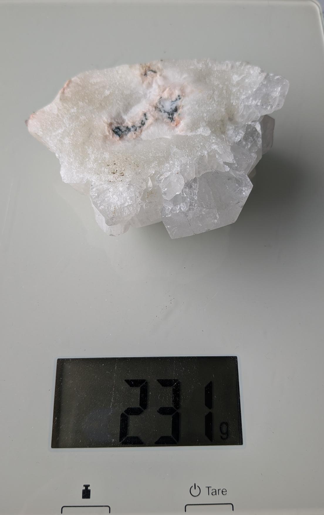 Een substantieel Apofylliet cluster van 231 gram uit Nasik, India, met heldere, glasachtige kristalstructuren op een perzikkleurige matrix, gefotografeerd op een digitale weegschaal.
