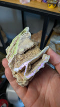 Een hand houdt een aura sphaleriet specimen vast, waarbij de glinsterende iriserende laag goed zichtbaar is.