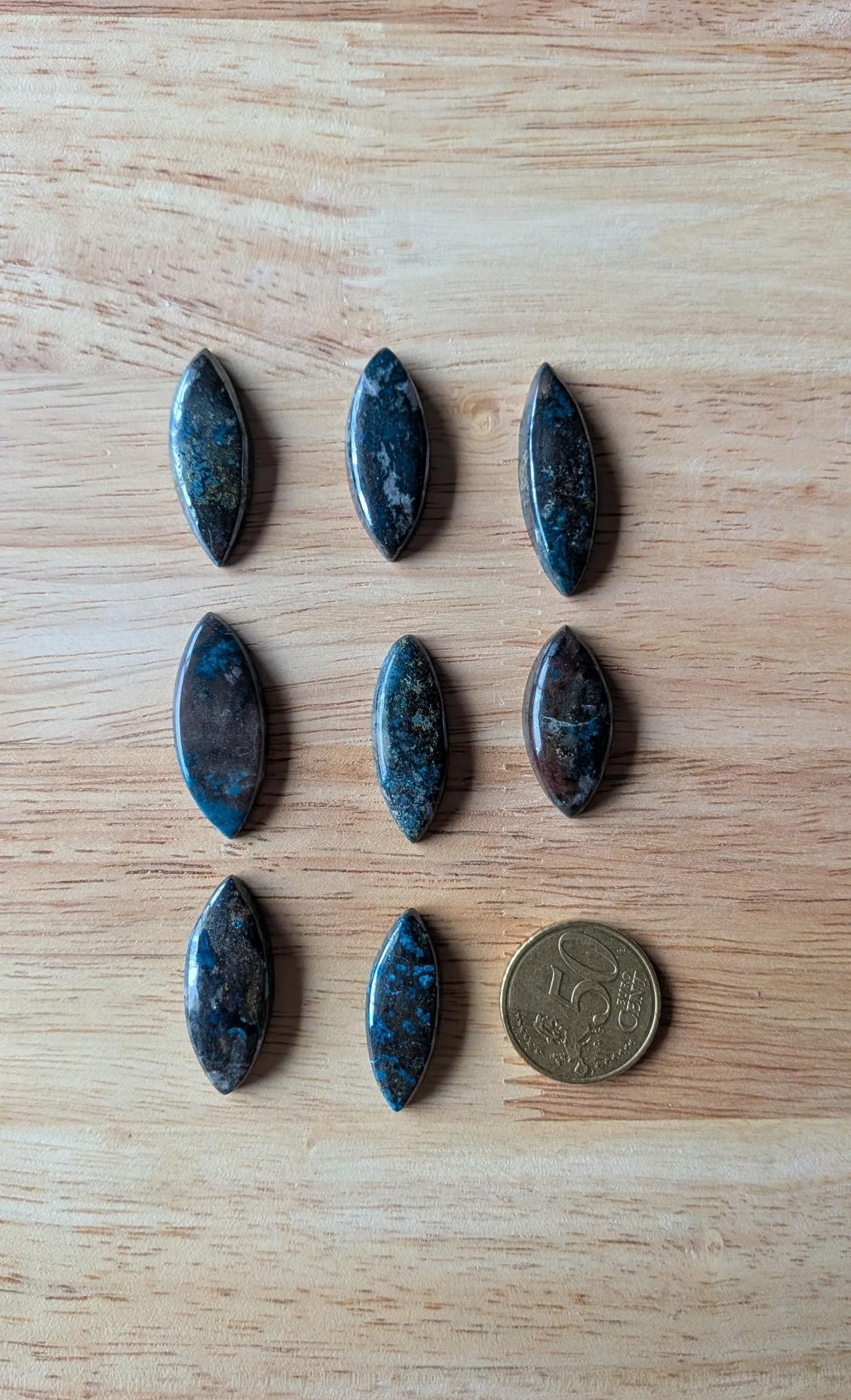 Acht navette-vormige diepblauwe Azuriet edelstenen op een houten achtergrond naast een 50 cent muntstuk voor de maatvoering.