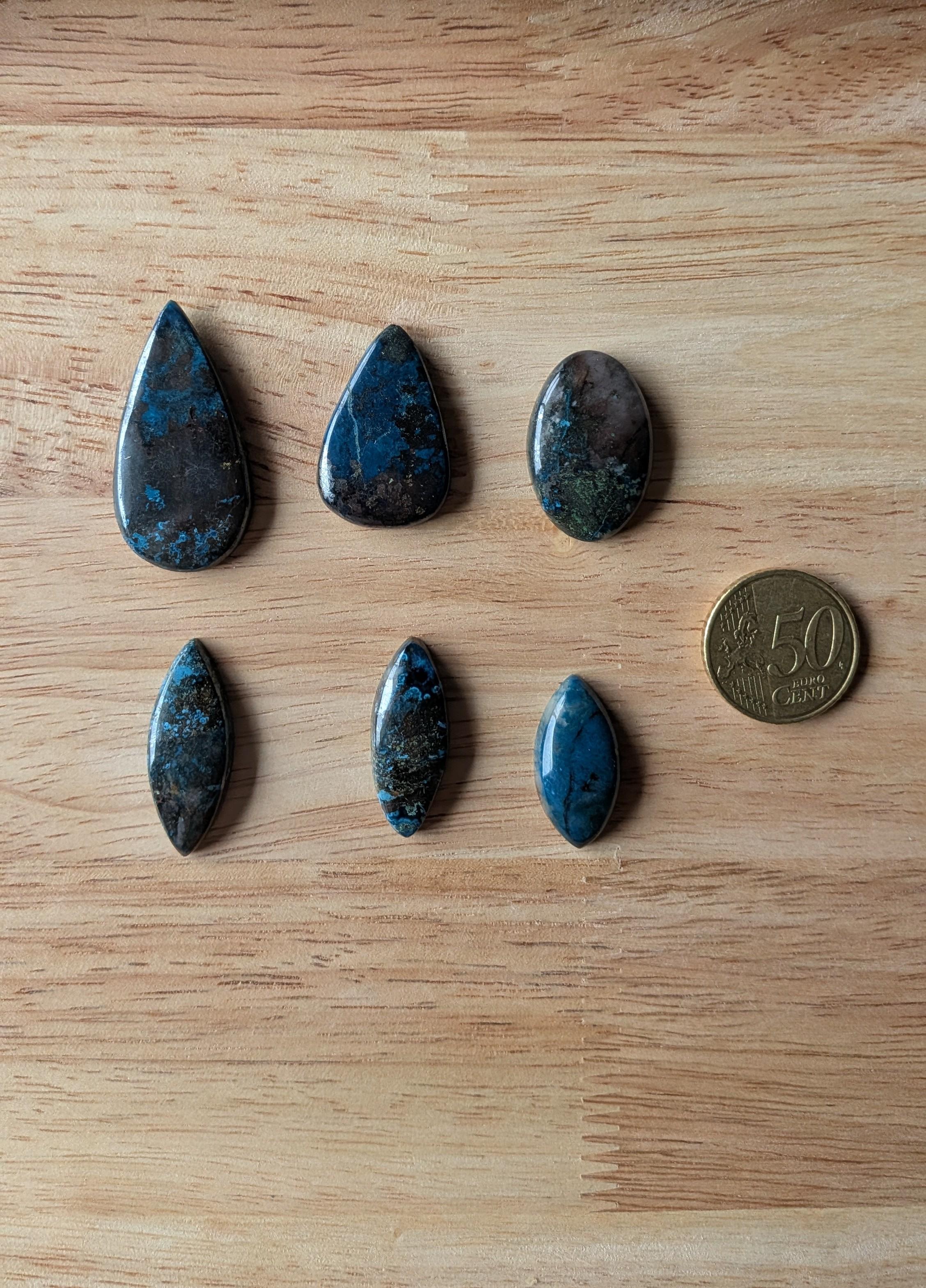 Zes gepolijste Azuriet Shattuckiet edelstenen in diverse vormen zoals druppel, ovaal en marquise naast een 50 eurocent munt voor een custom wire wrapped ontwerp.