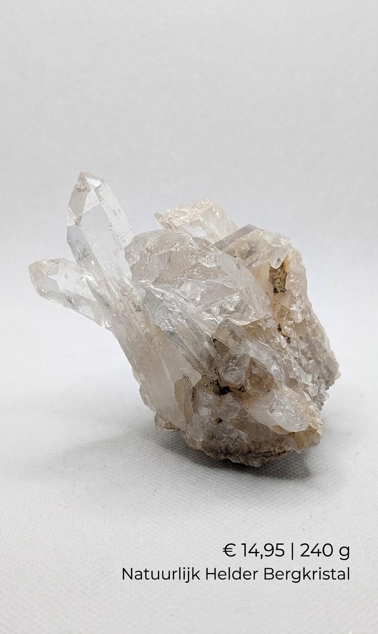 Een natuurlijk Bergkristal cluster van 240 gram met scherpe, heldere kristalpunten die schuin omhoog wijzen uit een fijnkorrelige, glinsterende basis op een egale, witte studio-achtergrond.