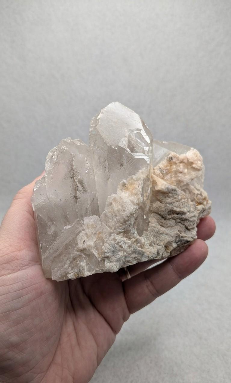 Een hand die een groot, natuurlijk Bergkristal cluster van 461 gram vasthoudt, met duidelijke, heldere kristaltoppen en een robuuste matrix aan de onderkant.