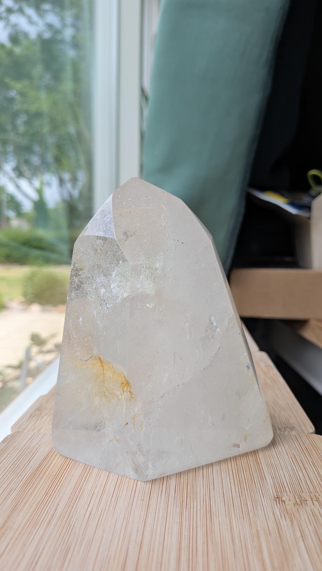 Een heldere, gepolijste bergkristal punt die staat op een houten ondergrond, met zichtbare natuurlijke insluitsels