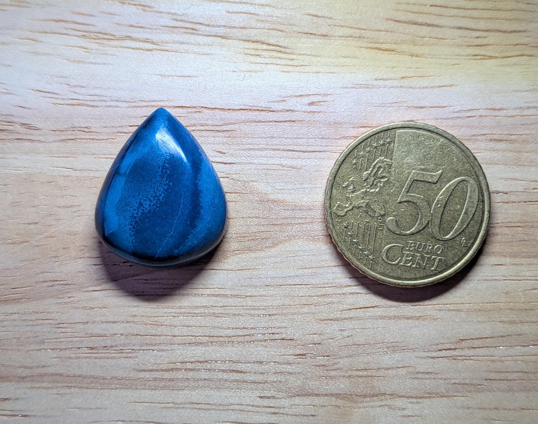 Diepblauwe Agaat edelsteen in druppelvorm met glad gepolijst oppervlak naast een 50 eurocent munt.
