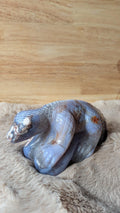 Handgesneden hagedis carving van blauwe bloemagaat met gedetailleerde schubben op een zachte achtergrond.