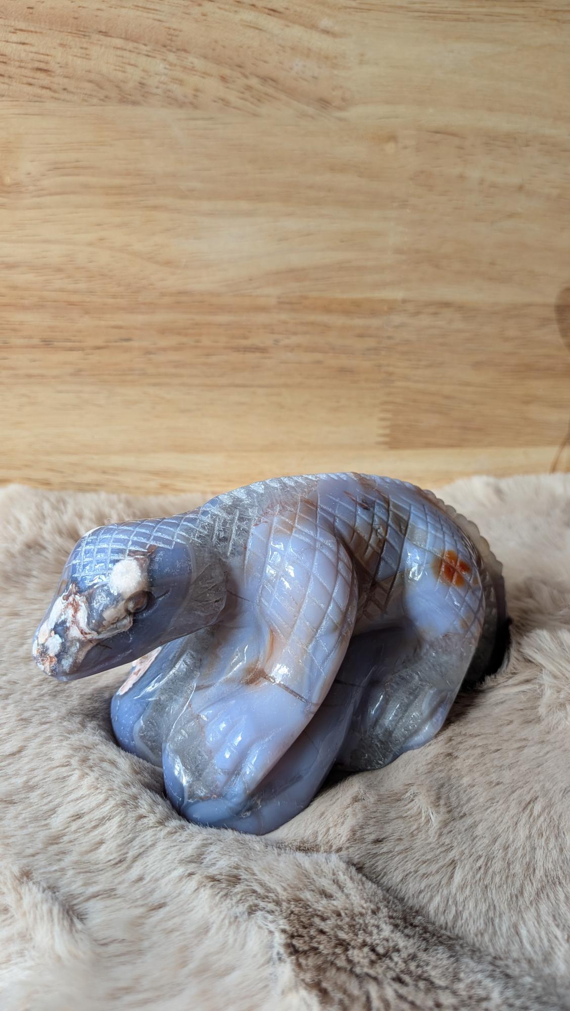 Handgesneden hagedis carving van blauwe bloemagaat met gedetailleerde schubben op een zachte achtergrond.